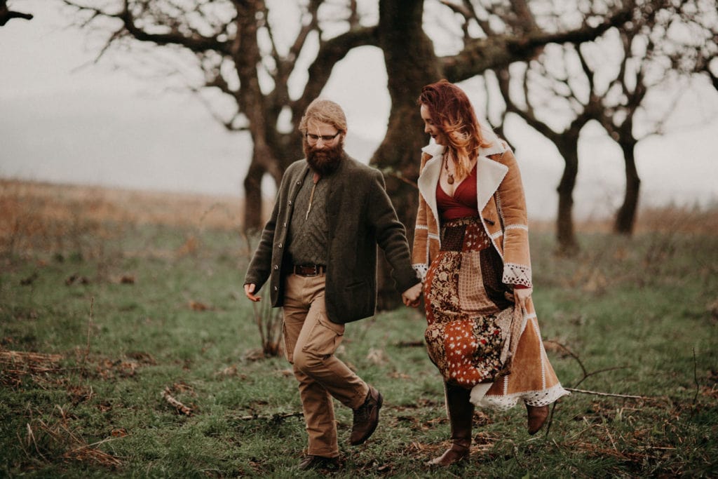 cute hippie boho couple walk hand in hand in forest Powell Butte Portland Engagement Photographer by Marcela Pulido Photography Portland Wedding Photographer