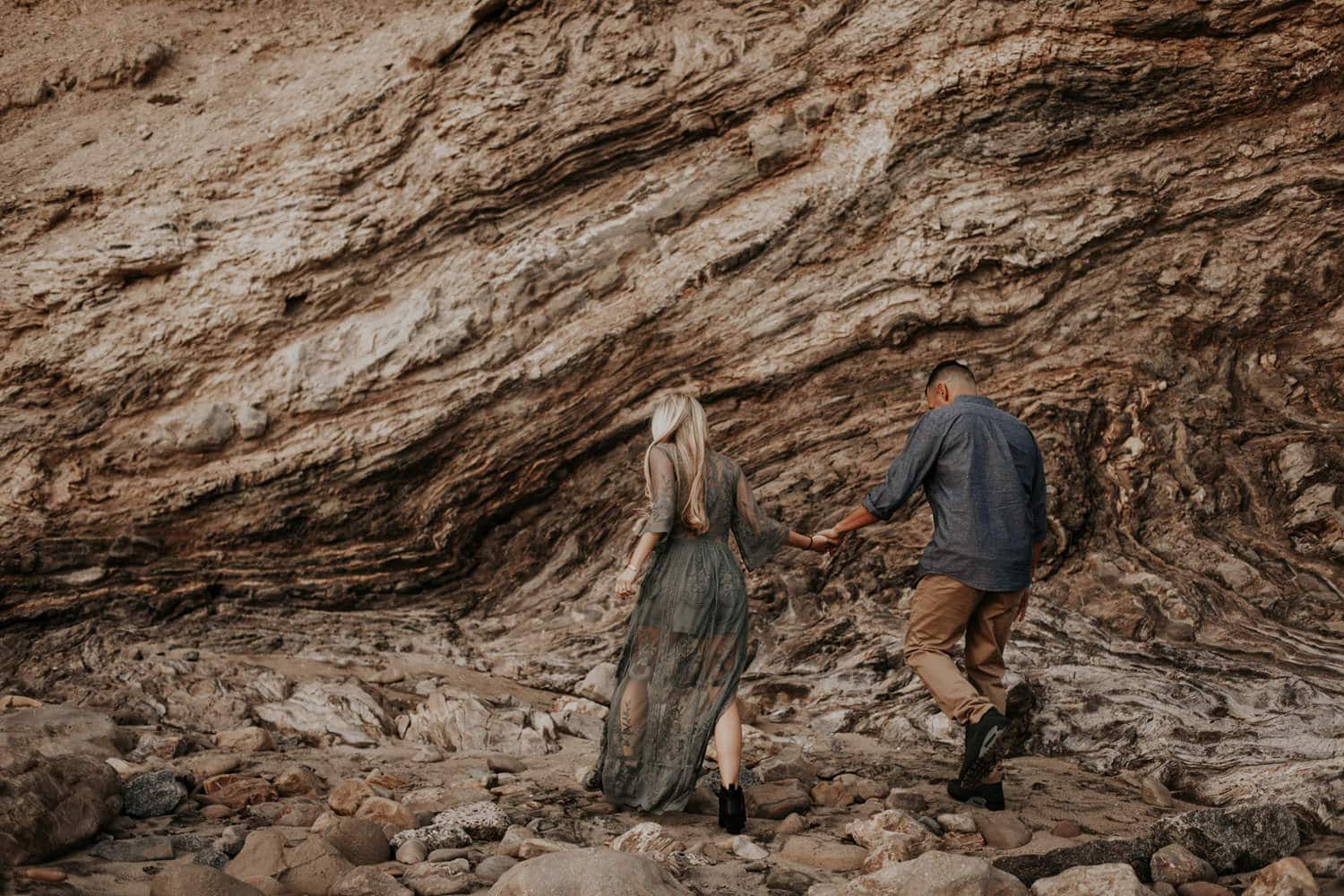 couple walking hand in hand on coast against cliff laguna beach engagement photographer