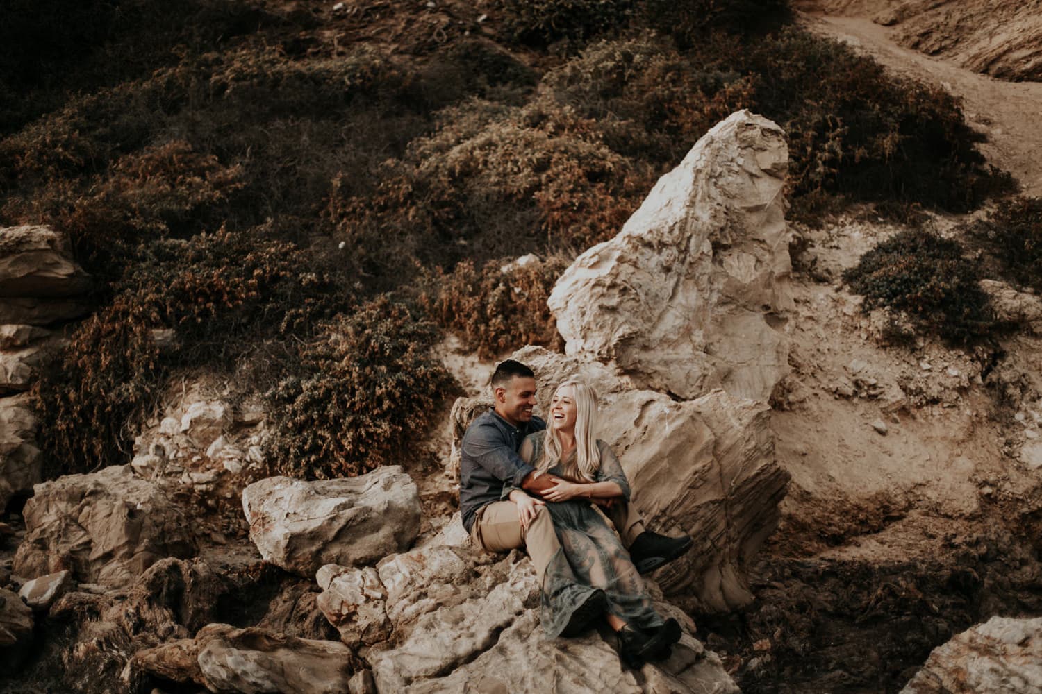 cute couple laughing sitting on rocks beach laguna beach engagement photographer