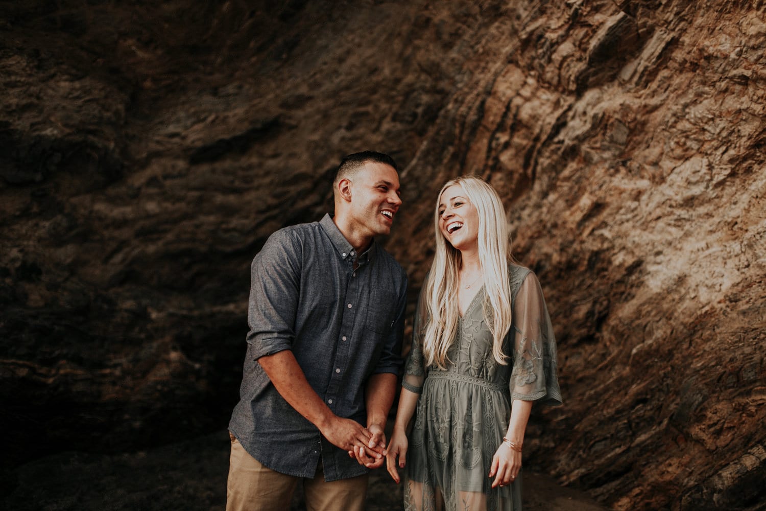 cute couple laughing together guy is wearing chambray shirt and girl in green dress long blonde hair laguna beach engagement photographer