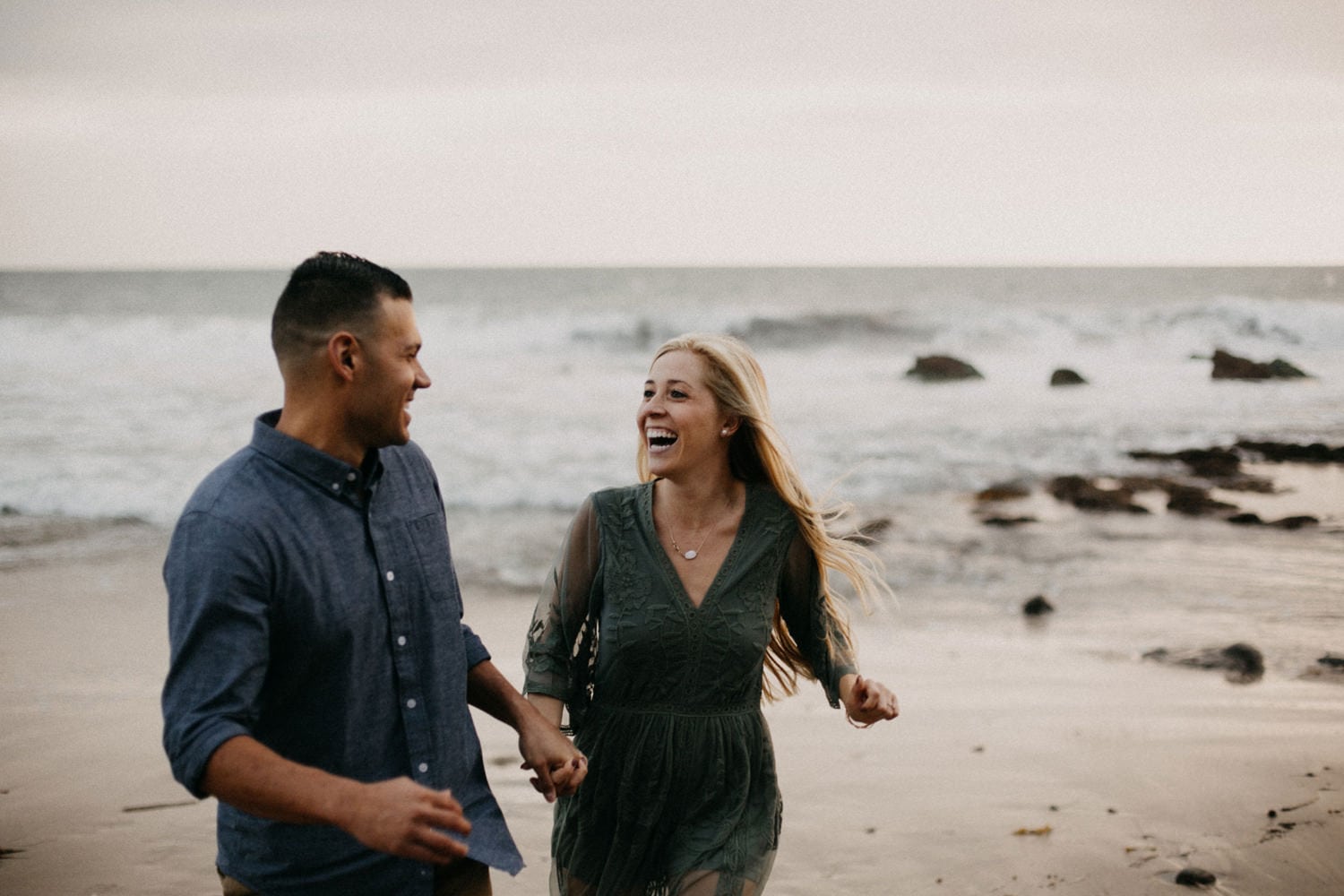 cute couple running and laughing blonde in green dress West Coast California sunset laguna beach engagement photographer