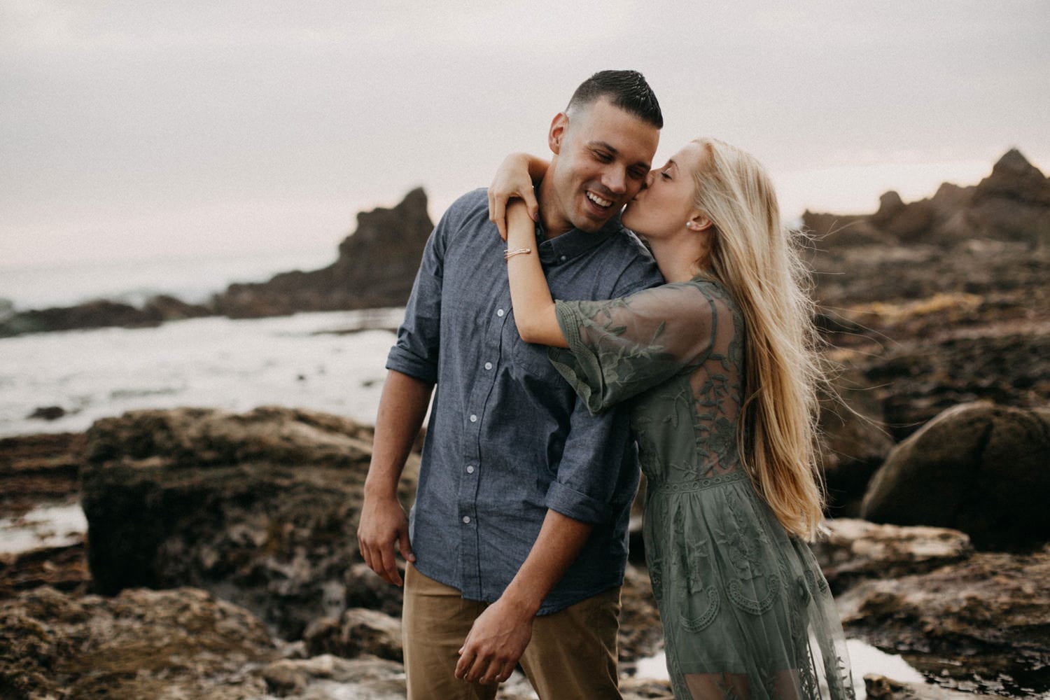 guy laughing while fiancee kisses her cheek on laguna beach engagement photographer