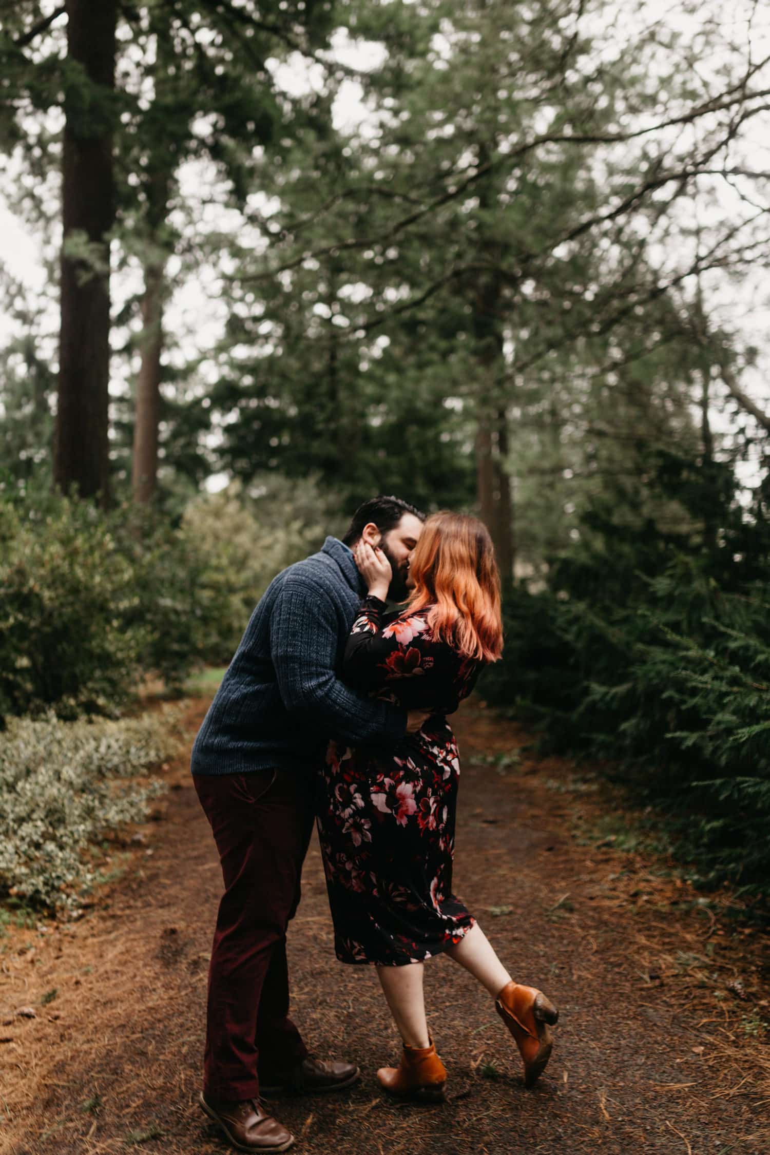 classic shot of couple kissing with the girl's foot popped up in the forest of Washington Park in Portland Oregon