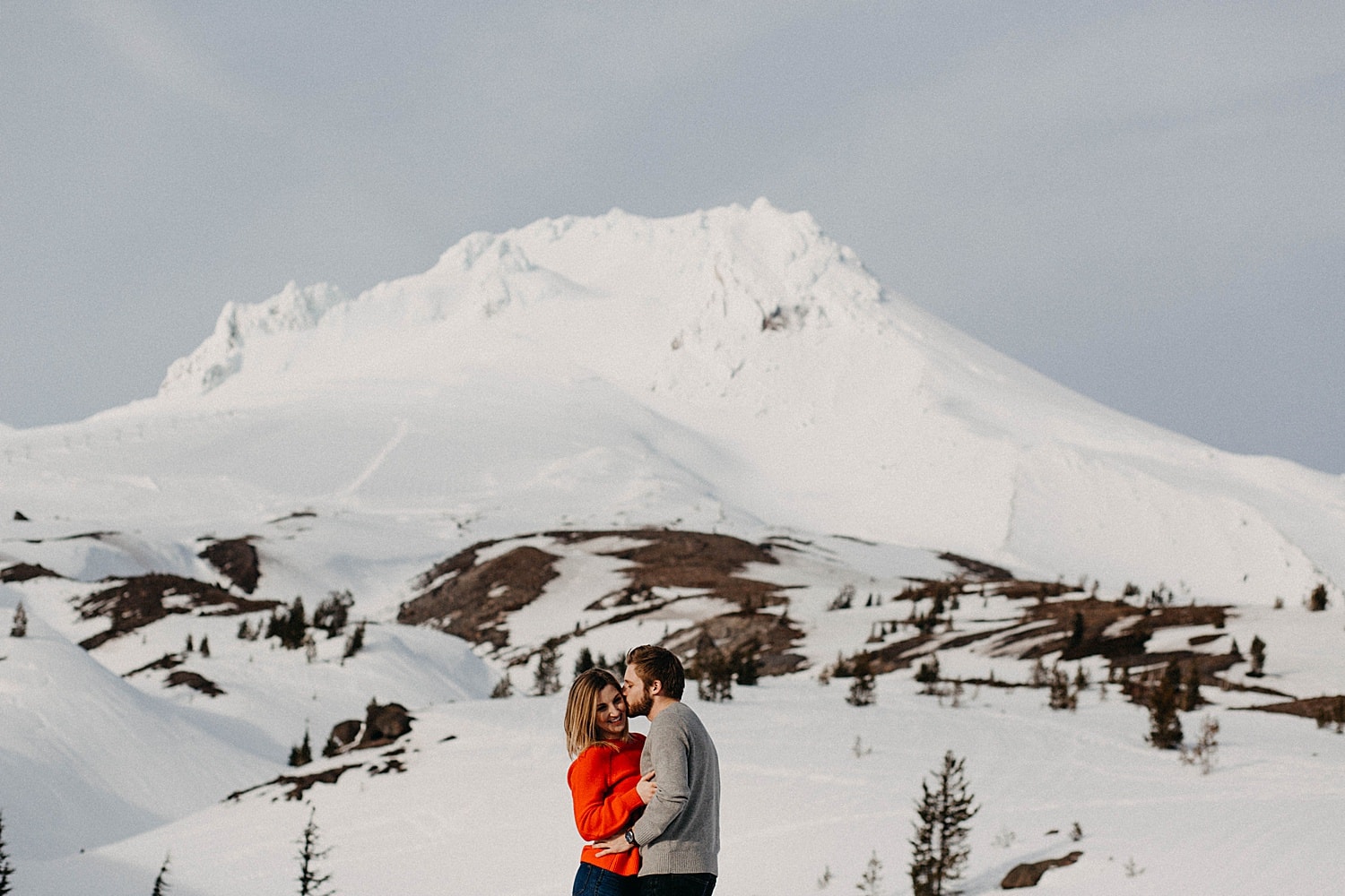 guy kissing girl on cheek in front of a snowy mt hood