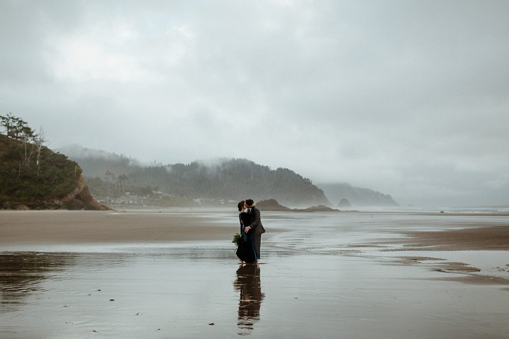 landscape shot of newlywed couple kissing on a foggy beach on the oregon coast hug point elopement captured by marcela pulido photography portland oregon wedding elopement photographer